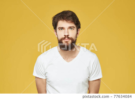 Brunette man on a yellow background in a white t-shirt cropped view Brunette man on a yellow background in a white t-shirt cropped view 77634084