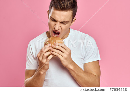 man with big hamburger on pink background calories fast food cropped view Copy Space close-up 77634318