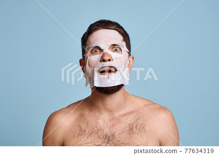 man in cleansing mask on blue background gesturing with hands naked torso cropped view 77634319