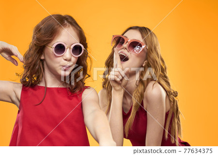 Happy sisters in red dresses on a yellow background are having fun and gesticulating Copy Space Happy sisters in red dresses on a yellow background are having fun and gesticulating Copy Space 77634375
