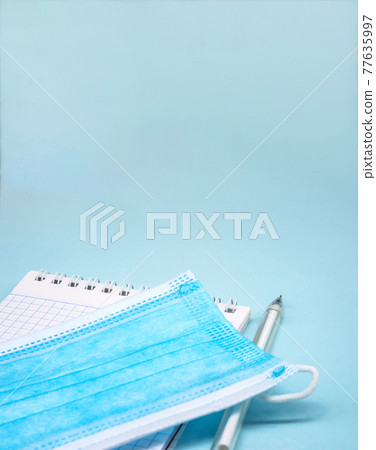 Medical mask and notepad on blue background. Stationery items and sanitary mask. Medical mask and notepad on blue background. Stationery items and sanitary mask. 77635997