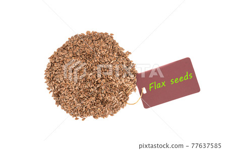 Pile of flax seeds on a white background and a label with the inscription Flax Seeds. 77637585
