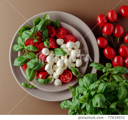 Caprese salad with tomato, mini mozzarella and basil on a brown background. Caprese salad with tomato, mini mozzarella and basil on a brown background. 77639032