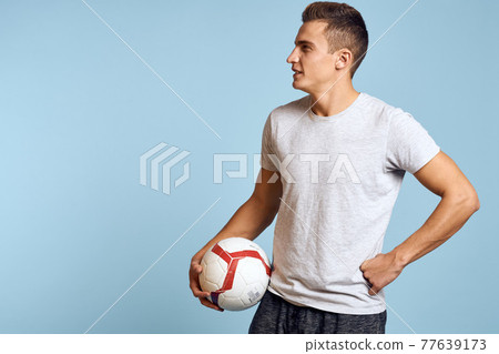 Happy guy with soccer ball in hand on blue background plays soccer cropped view 77639173