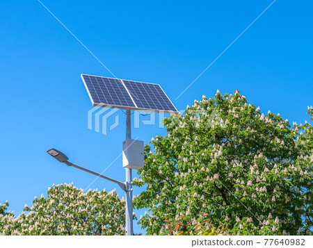 A street lamp and a solar panel against a blue sky. 77640982