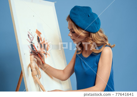 Woman artist paintbrush paint on canvas easel art education blue background Woman artist paintbrush paint on canvas easel art education blue background 77641641
