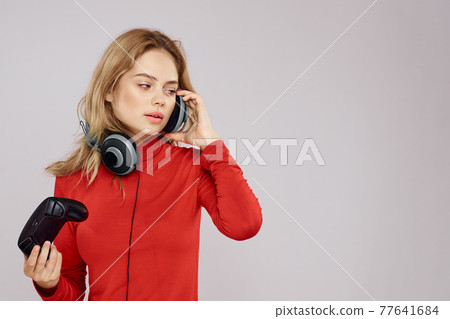 Woman with headphones controller in hands a console game fun leisure red jacket lifestyle light background Woman with headphones controller in hands a console game fun leisure red jacket lifestyle light background 77641684
