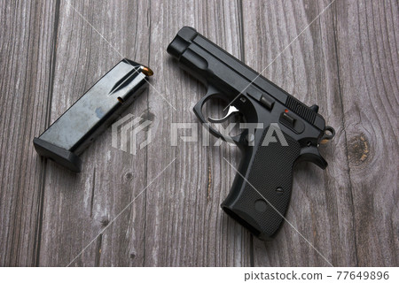 Still life with black handgun with cartridge magazine on old grungy brown wooden background, Black semi-automatic pistol on wood table Still life with black handgun with cartridge magazine on old grungy brown wooden background, Black semi-automatic pistol on wood table 77649896