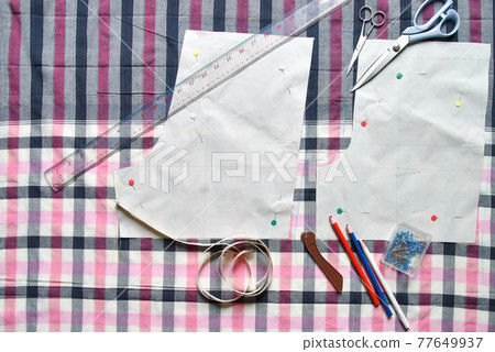 Sewing supplies on a draft paper of pants on fabric, sewing thread, scissors, , colorful pen, pencil, ruler, centimeter tape, spool of thread and equipment Sewing supplies on a draft paper of pants on fabric, sewing thread, scissors, , colorful pen, pencil, ruler, centimeter tape, spool of thread and equipment 77649937