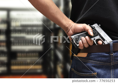 A man pulls out a gun tucked in his pant rear view with blurred department store background, a concept of city crime social issue A man pulls out a gun tucked in his pant rear view with blurred department store background, a concept of city crime social issue 77650253