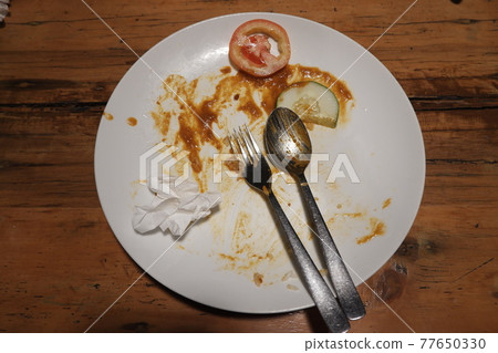 Top view of dirty plate that contain sauce with a slice of tomato and cucumber on it. Dirty plate with spoon and fork on it after meal is finished. Top view of dirty plate that contain sauce with a slice of tomato and cucumber on it. Dirty plate with spoon and fork on it after meal is finished. 77650330