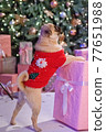Dog in santa costume is sitting under christmas tree with gifts in studio 77651988
