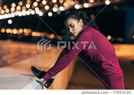 Fit woman stretching her body during a workout at night 77653530