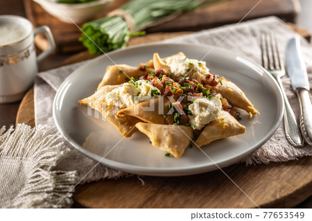 Fried pierogi served on a plate with bryndza cheese, bacon, and chives Fried pierogi served on a plate with bryndza cheese, bacon, and chives 77653549