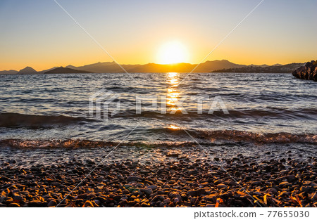 Beautiful sunset on the Mediterranean coast with islands and mountains. Stones on the beach lit by sunlight 77655030
