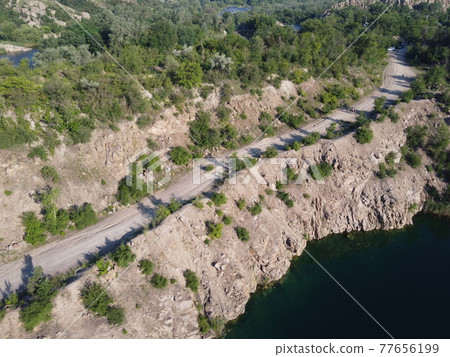 Rocky shore of the Radon Lake on a sunny summer morning. Aerial view of an old flooded granite quarry. A picturesque pond. Rocky shore of the Radon Lake on a sunny summer morning. Aerial view of an old flooded granite quarry. A picturesque pond. 77656199