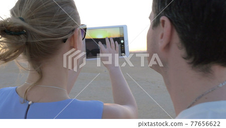 Young people on beach shooting sunset with pad 77656622