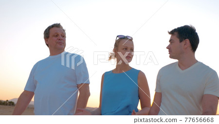 Three people enjoying evening walk on the beach 77656668