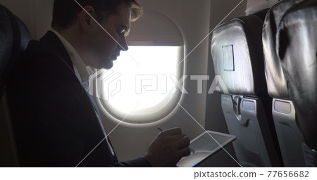 Young businessman working with pad in plane 77656682