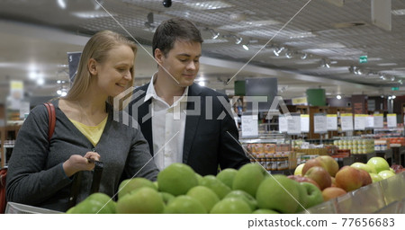 Couple Choosing Apples in Grocery Store 77656683