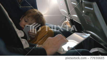 Child with cell and and man using pad in plane Child with cell and and man using pad in plane 77656685