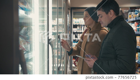 Young couple taking frozen food from fridge in the shop 77656725