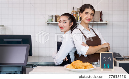 The shopkeeper and barista stand  smiling with arms folded in front of a coffee shop counter. Morning atmosphere in a coffee shop. 77658358