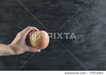 Farmer holding a yellowish redish apple between fingers Farmer holding a yellowish redish apple between fingers 77658965