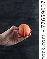 Holding a red peach and tapping on it on black background 77659037