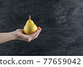 A person holding a yellow pear in the palm 77659042