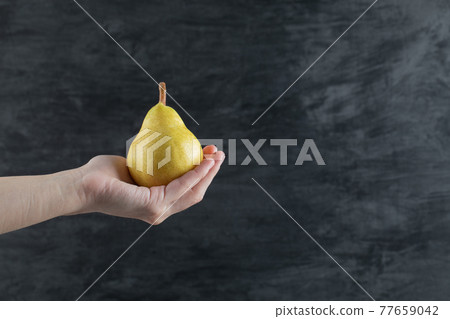 A person holding a yellow pear in the palm 77659042