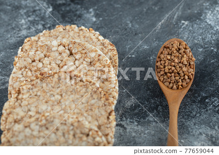 Airy crispbread and wooden spoon of raw buckwheat on marble surface 77659044