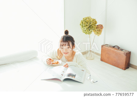 A girl eating a snack but looking at a magazine A girl eating a snack but looking at a magazine 77659577