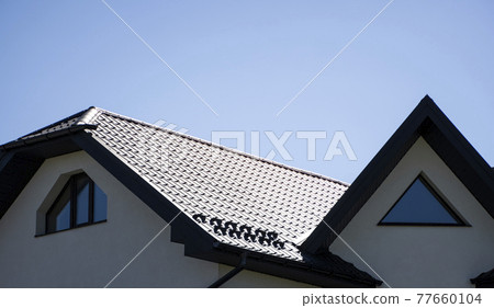 Brown corrugated metal profile roof installed on a modern house. The roof of corrugated sheet. Roofing of metal profile wavy shape. Modern roof made of metal. Metal roofing. Brown corrugated metal profile roof installed on a modern house. The roof of corrugated sheet. Roofing of metal profile wavy shape. Modern roof made of metal. Metal roofing. 77660104
