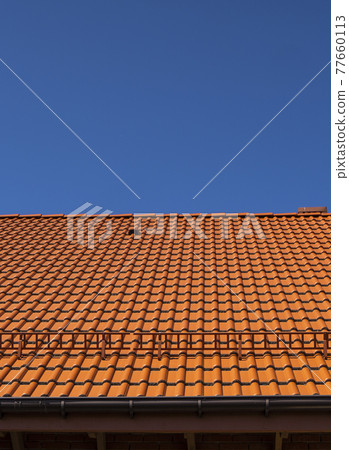 Red corrugated metal profile roof installed on a modern house. The roof of corrugated sheet. Roofing of metal profile wavy shape. Modern roof made of metal. Metal roofing. 77660113