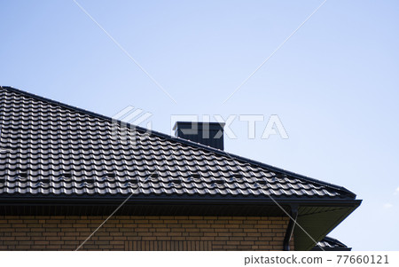 Brown corrugated metal profile roof installed on a modern house. The roof of corrugated sheet. Roofing of metal profile wavy shape. Modern roof made of metal. Metal roofing. Brown corrugated metal profile roof installed on a modern house. The roof of corrugated sheet. Roofing of metal profile wavy shape. Modern roof made of metal. Metal roofing. 77660121