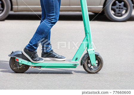 A modern concept on mobile electric transport: a person rides an electric scooter along the carriageway of a city street. A modern concept on mobile electric transport: a person rides an electric scooter along the carriageway of a city street. 77660600