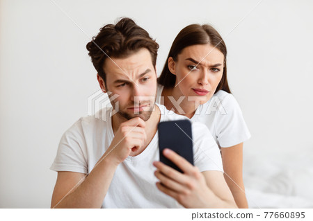 Jealous Woman Reading Husband's Message On Phone Behind Back Indoors Jealous Woman Reading Husband's Message On Phone Behind Back Indoors 77660895