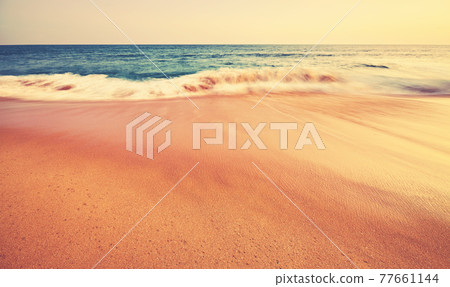 Tropical sandy beach with motion blurred waves at sunset, focus on foreground, color toning applied Tropical sandy beach with motion blurred waves at sunset, focus on foreground, color toning applied 77661144