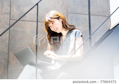 A woman using a laptop on a bright staircase with plenty of sunlight A woman using a laptop on a bright staircase with plenty of sunlight 77664373