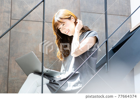 A woman using a laptop on a bright staircase with plenty of sunlight 77664374