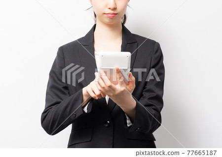 A business woman standing in front of a white background and using a calculator A business woman standing in front of a white background and using a calculator 77665187