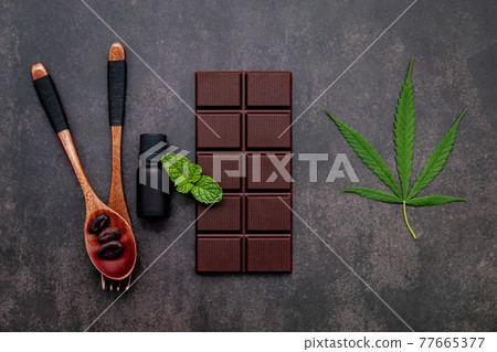 Food conceptual image of cannabis leaf with dark chocolate and fork set up on dark concrete background. Food conceptual image of cannabis leaf with dark chocolate and fork set up on dark concrete background. 77665377