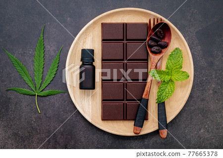 Food conceptual image of  cannabis leaf  with dark chocolate and fork set up on dark concrete background. 77665378
