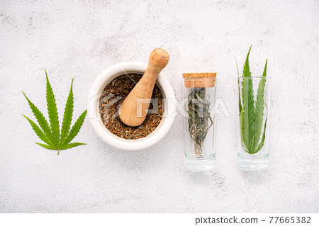 Glass bottle of cannabis oil with white mortar and hemp leaves set up on concrete background. Glass bottle of cannabis oil with white mortar and hemp leaves set up on concrete background. 77665382