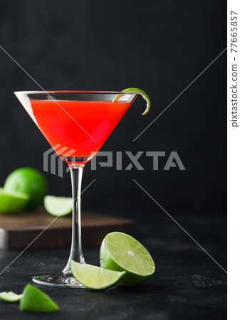 Cosmopolitan cocktail in classic crystal glass with lime peel and fresh limes on black background. 77665857