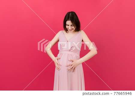 Happy pregnant woman touching her abdomen at Colored background. Future mother. Expecting of a baby. Copy space Happy pregnant woman touching her abdomen at Colored background. Future mother. Expecting of a baby. Copy space 77665946