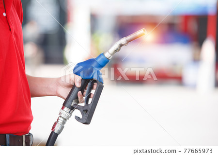 hand of man holding pump nozzle for service at gas station. male employee worker fueling oil car. 77665973