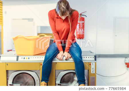 Woman sits on washing machine in laundromat Woman sits on washing machine in laundromat 77665984