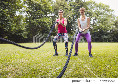 Smiling young women doing battle rope exercise in park Smiling young women doing battle rope exercise in park 77665998